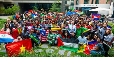 Photo taken from above, looking down at a crowd of people smiling and holding up the flags of several countries form around the world.