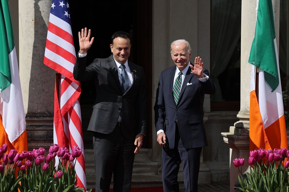 two men outside waving in between American and Irish flags