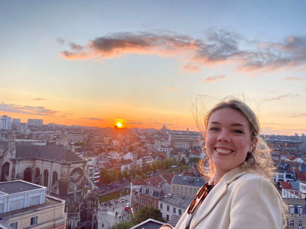 Headshot of Róisín de Bhaldraithe in front of the Brussels skyline.