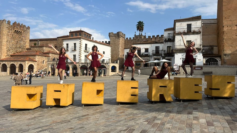 Irish dancers standing on yellow bricks that spell the name of the city Caceres