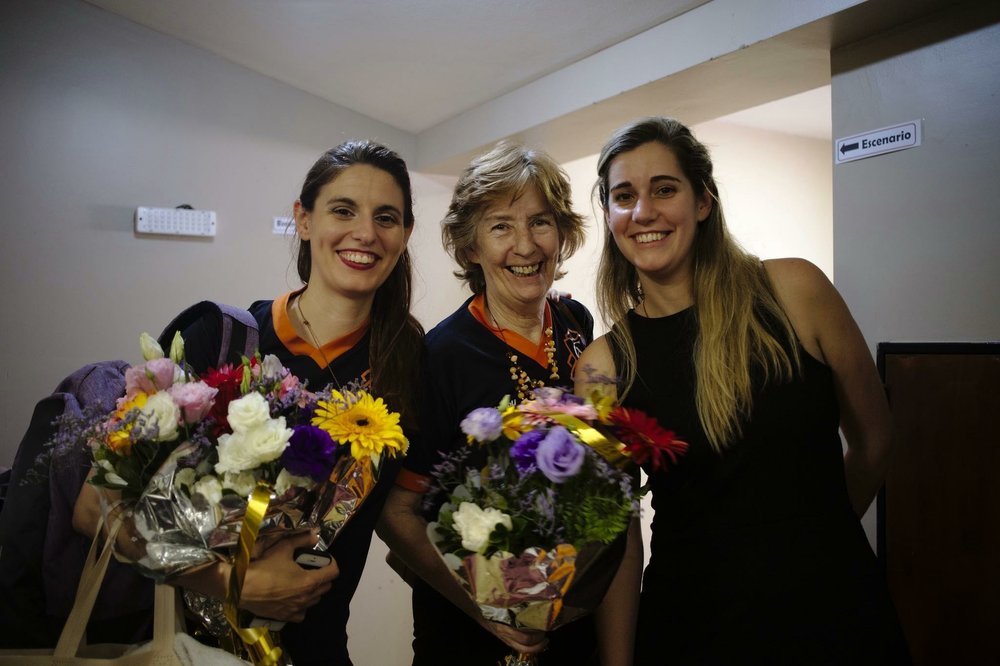 three women posing with flowers and smiling