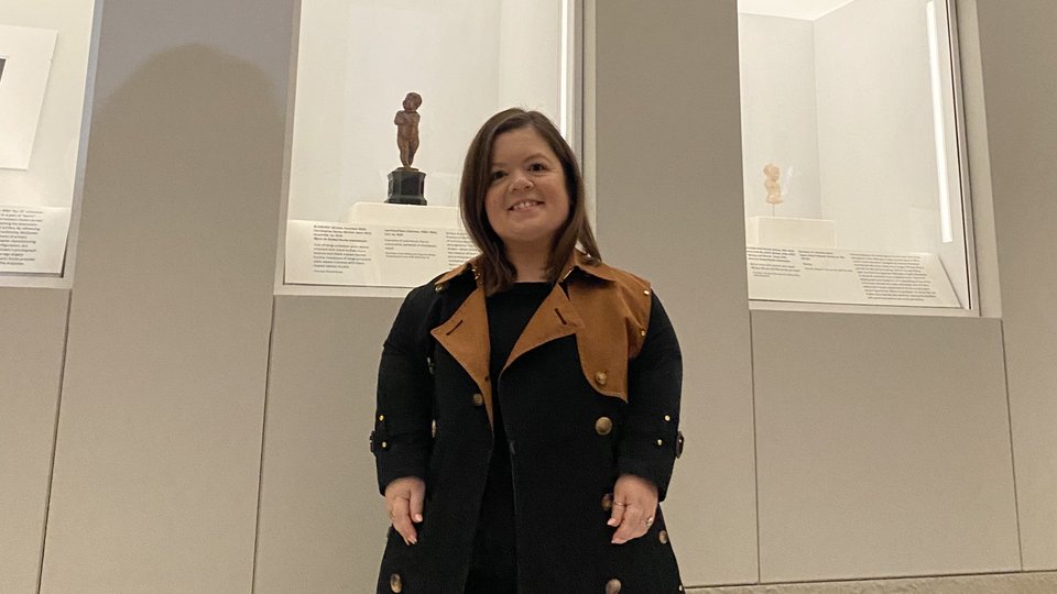 Sinéad Burke posing beneath mannequins wearing her donated garments at the Costume Art exhibition