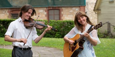 A man and woman playing violin and guitar outdoors.