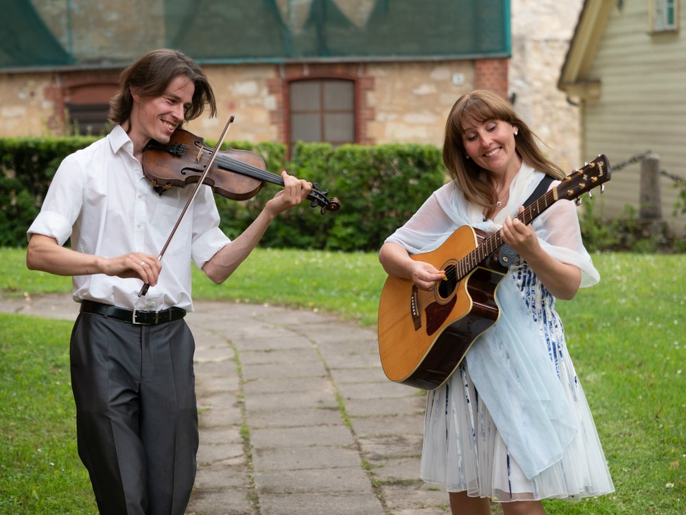 A man and woman playing violin and guitar outdoors.