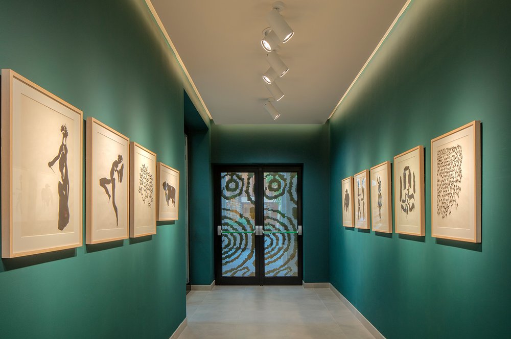 A green hued exhibition space featuring black and white lithographic brush artwork on the walls.