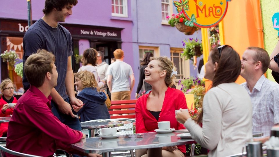 Four people sitting at an outdoor cafe table, interacting with a waiter.