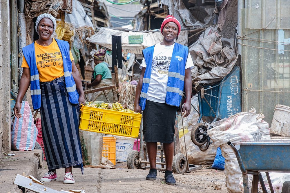Two volunteers carrying a yellow basket fully of bananas.