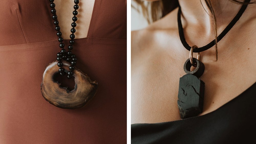 Examples of wearable art made of bog oak, two statement necklaces show natural forms of wood, one hands from a beaded cord, the other from a gold hoop on a shorter black cord