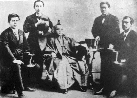 Group of 5 men sitting on chairs in suits