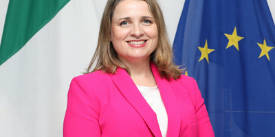 Headshot of Marianne Bolger standing in front of Irish and EU flags