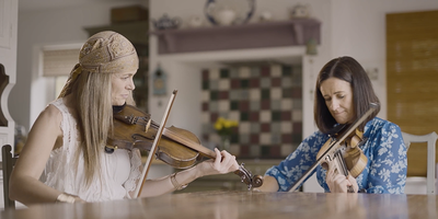 two women playing the fiddle at a kitchen table
