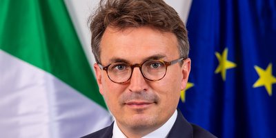 Ambassador Luke Feeney standing in front of Irish and EU flags