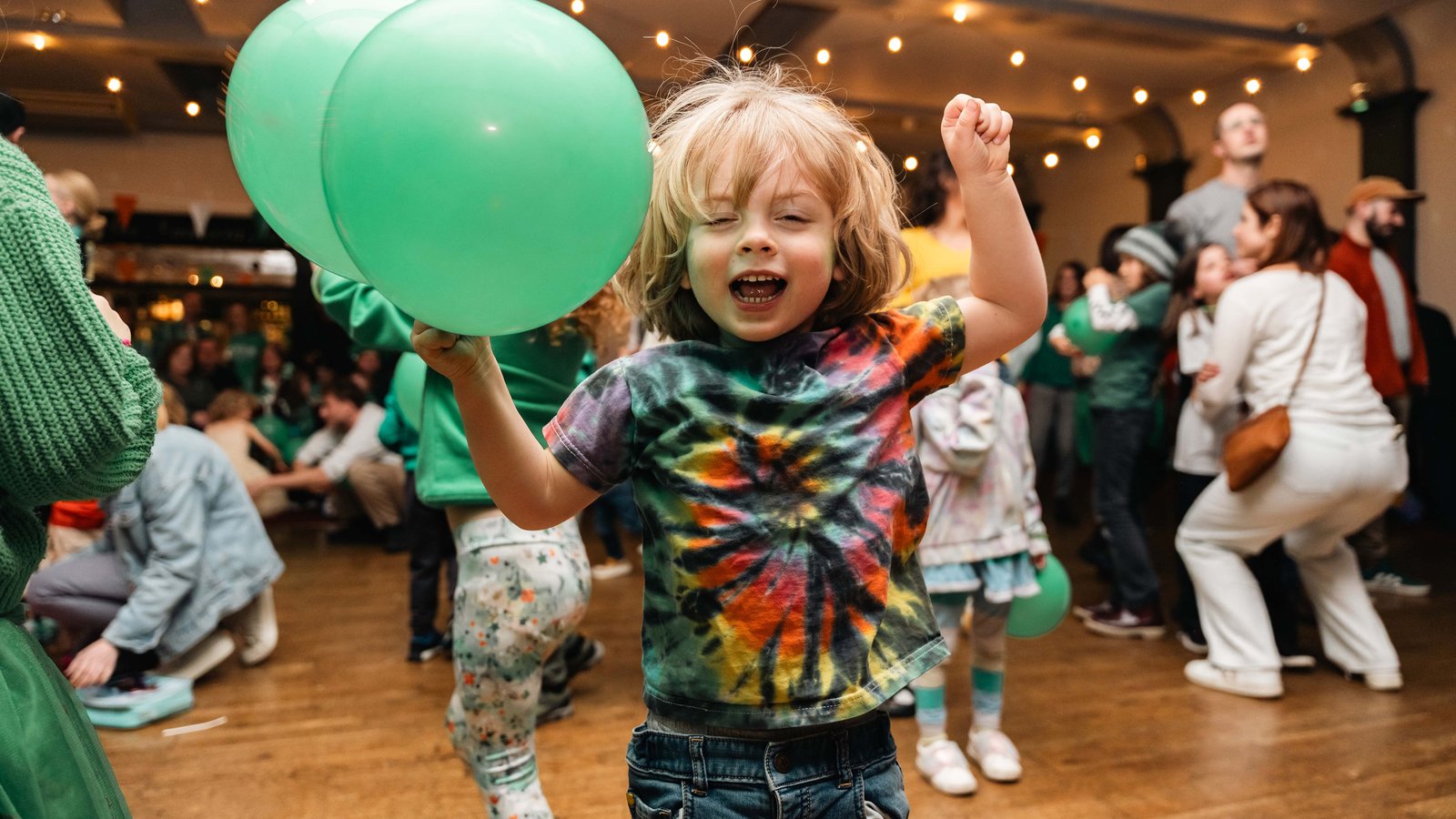 A child jumping for joy holding two green balloons