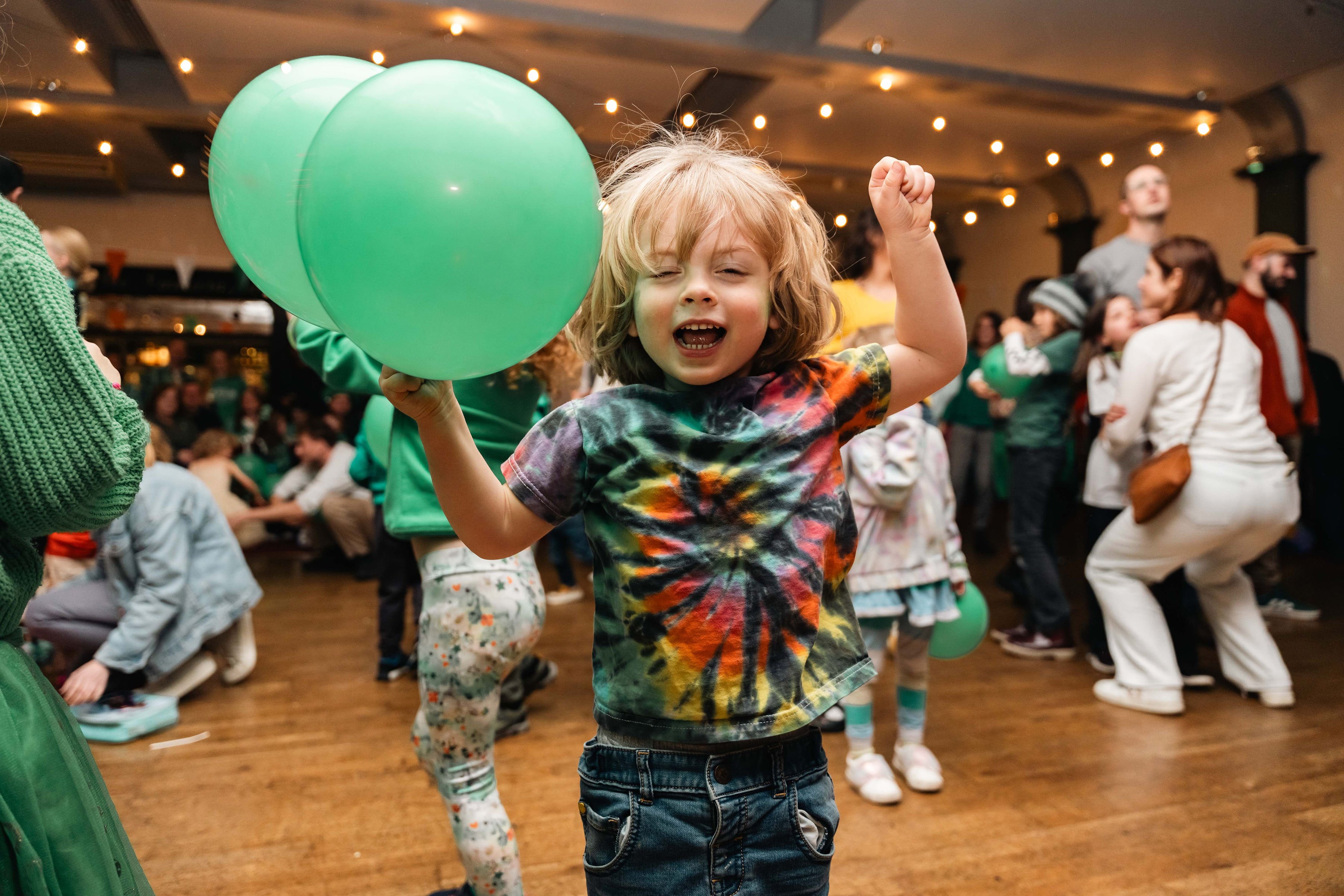 A child jumping for joy holding two green balloons