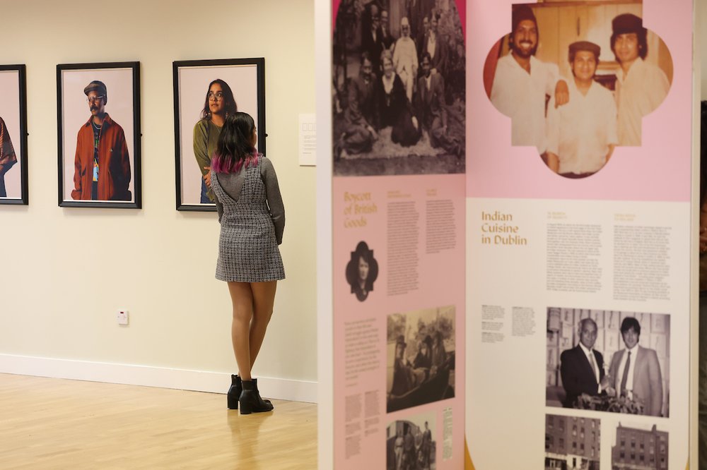 A woman looking at portraits, with an exhibition panel in the foreground of the photo.