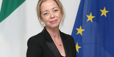 Ambassador Marcella Smyth standing in front of the Irish, EU and Latvian flags.