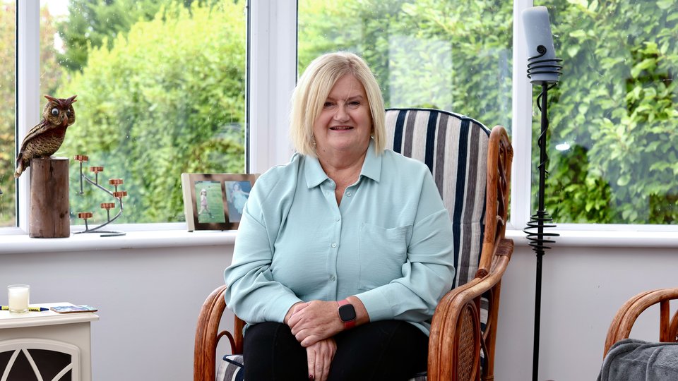 Woman sitting in a chair in a conservatory smiling at the camera