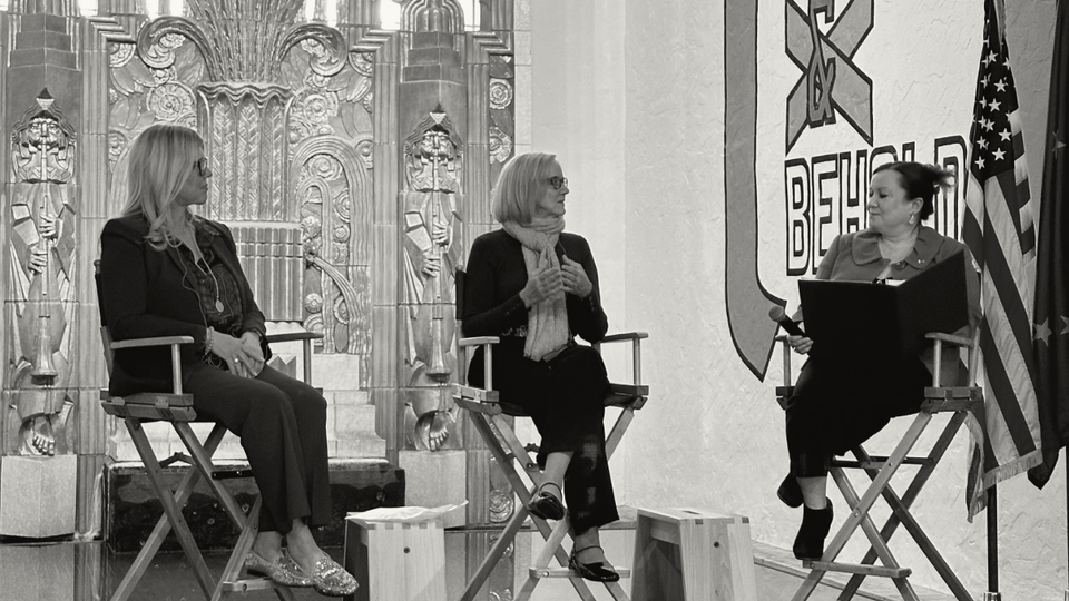 Three women sitting on chairs on a stage talking