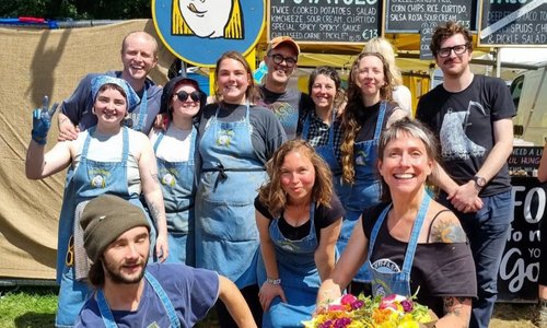 12 members of the My Goodness Food team pose together with menu items in the sunshine outside their food truck
