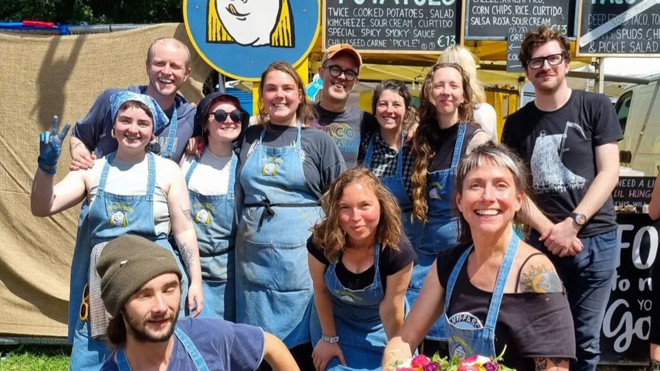 12 members of the My Goodness Food team pose together with menu items in the sunshine outside their food truck