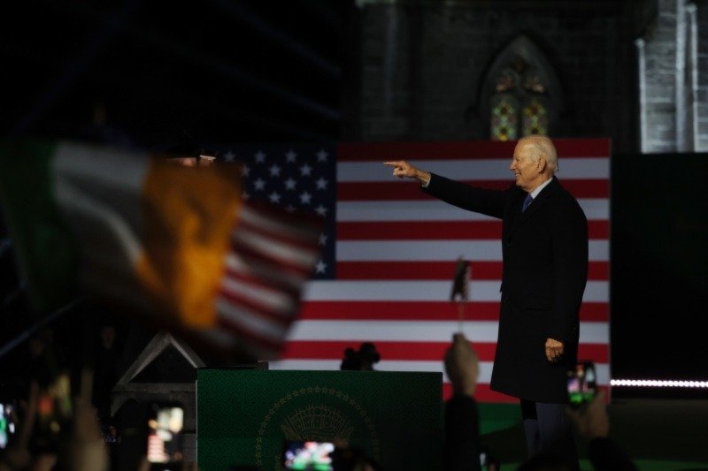 man pointing on stage lit up from below in front of an american flag