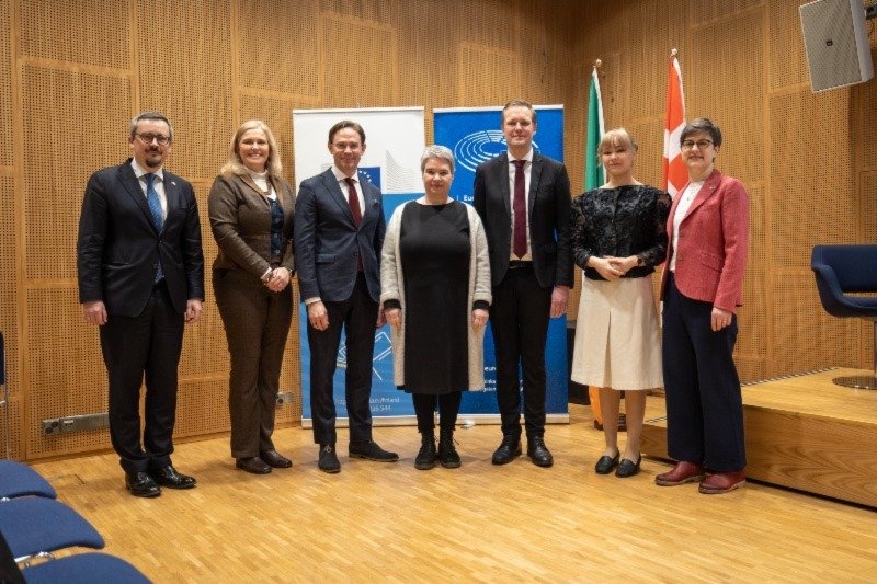 seven men and women standing posing for a photo in suits and office wear
