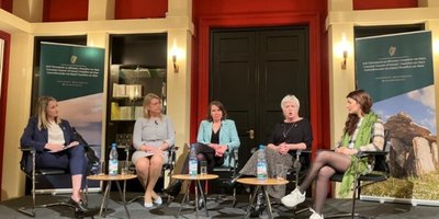 five women sitting down on a stage for a panel discussion, one woman is talking