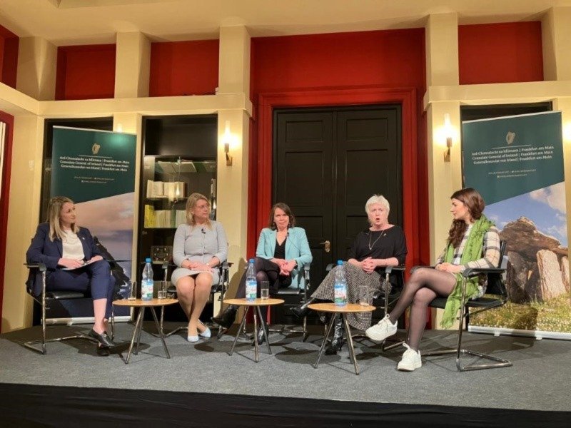 five women sitting down on a stage for a panel discussion, one woman is talking