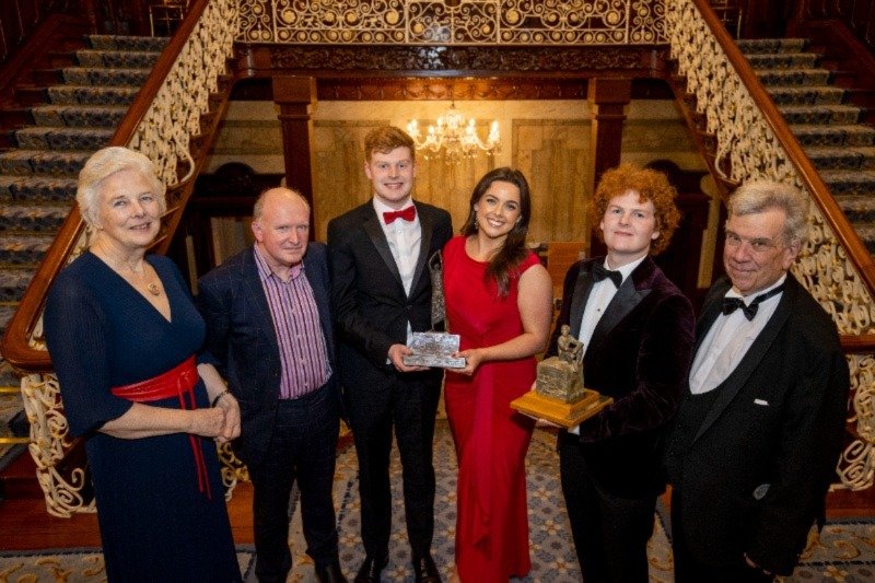 six men and women standing posing for a photo in black tie attire on the landing of a dual way staircase