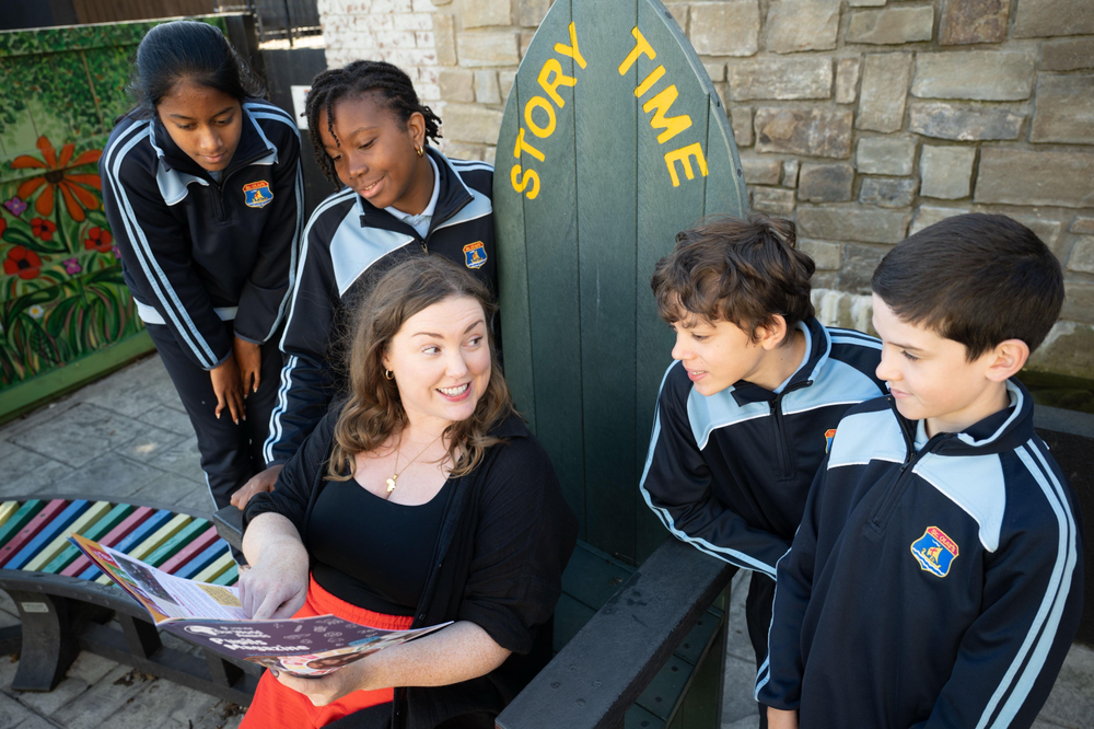 lady sitting on a large chaire telling children a story with 4 children gathered around her