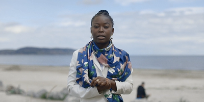 Woman standing on the beach wearing blue scarf and white shirt