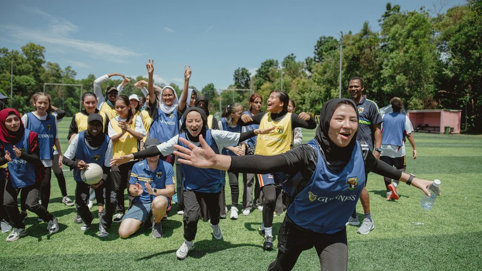 A group of teenagers from different ethnic backgrounds in yellow and blue sports bibs, running happily toward the camera