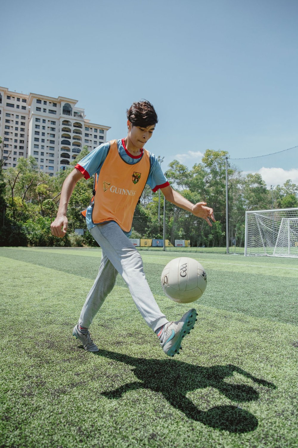 A teenage boy practicing his solo kicks with a gaelic football