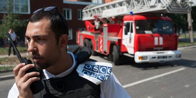 A man speaking into a walkie talkie in front of a fire engine.