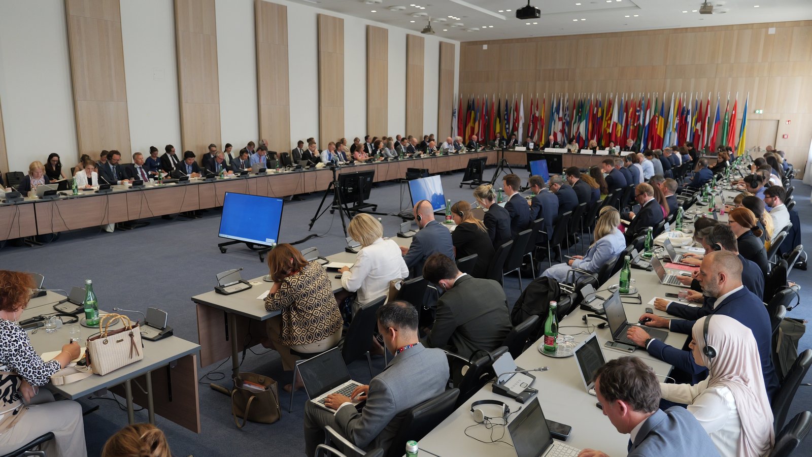 A collection of people sitting a tables with country flags behind them