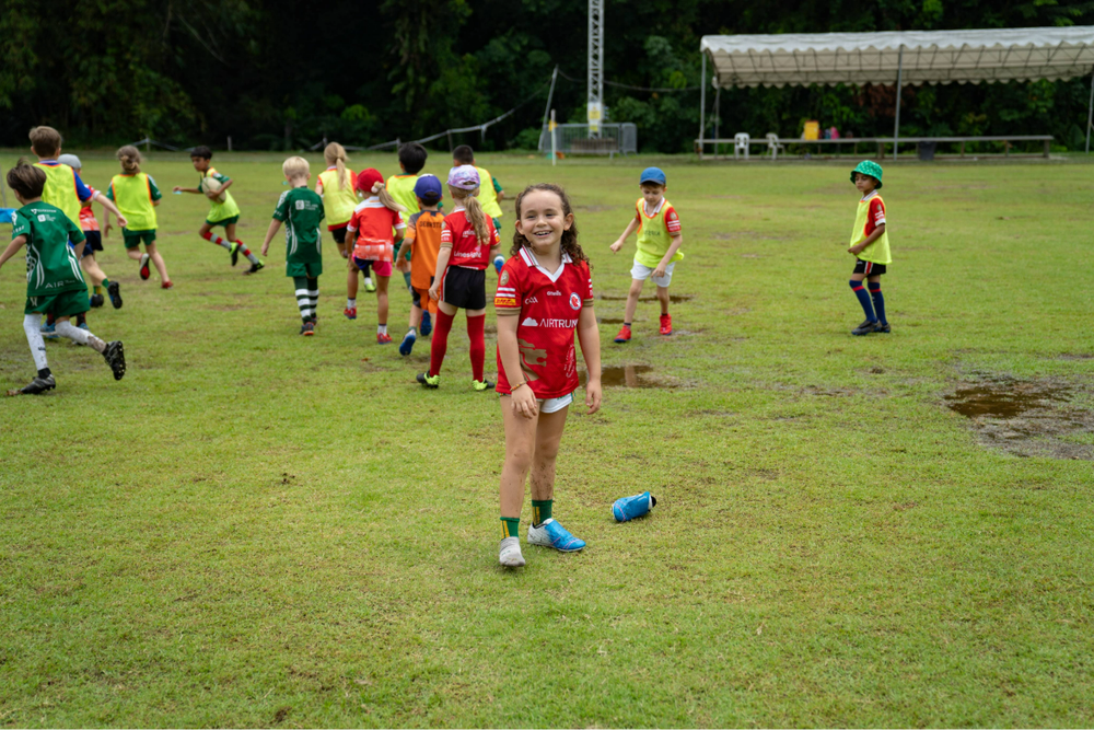 A young girl with only one football boot on, smiling for the camera on the pitch