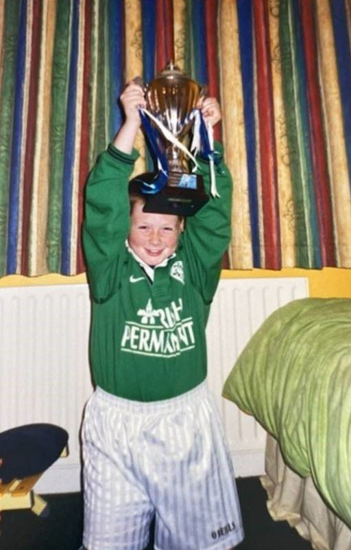 A young boy wearing an Irish rugby jersey holding up a trophy