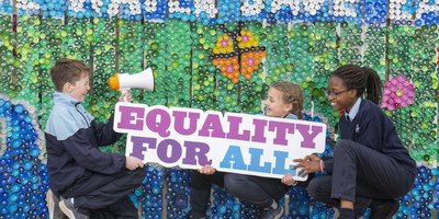 Three crouching schoolchildren hold a sign saying: equality for all.