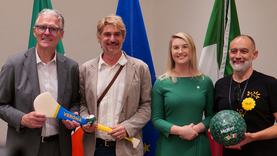 Men and women holding footballs and hurleys