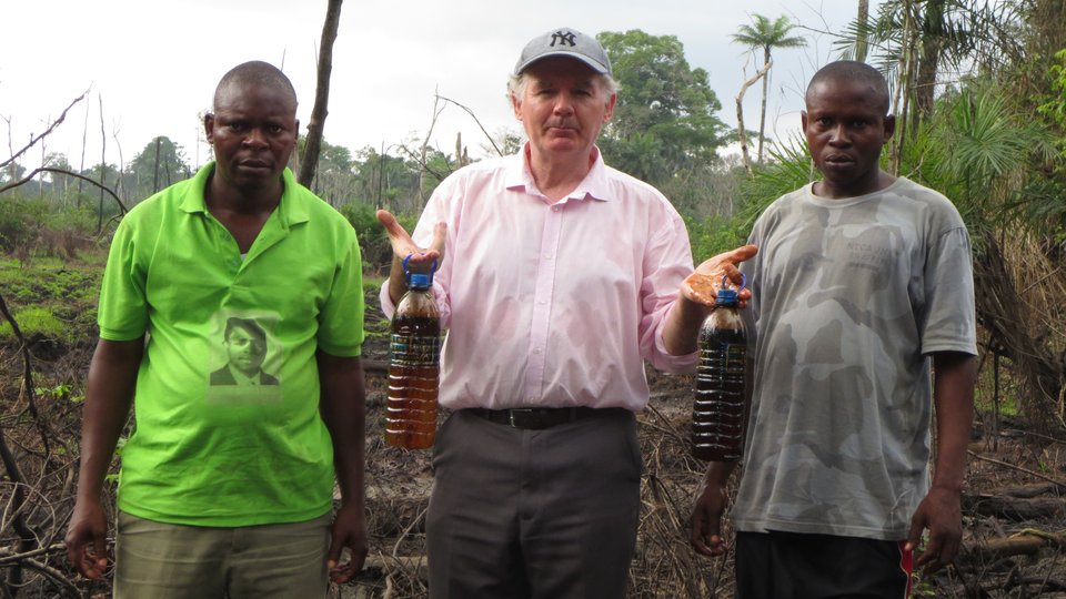Fr O' Hara standing with two companions showing bottles of collected oil