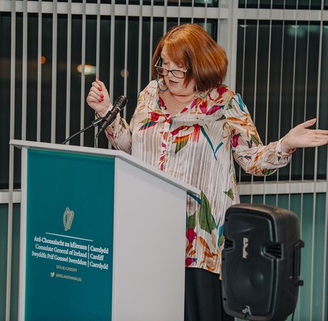 Red haired woman gesticulating widely while speaking at a podium