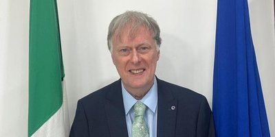 Ambassador Patrick McManus standing in front of the Irish and EU flags.