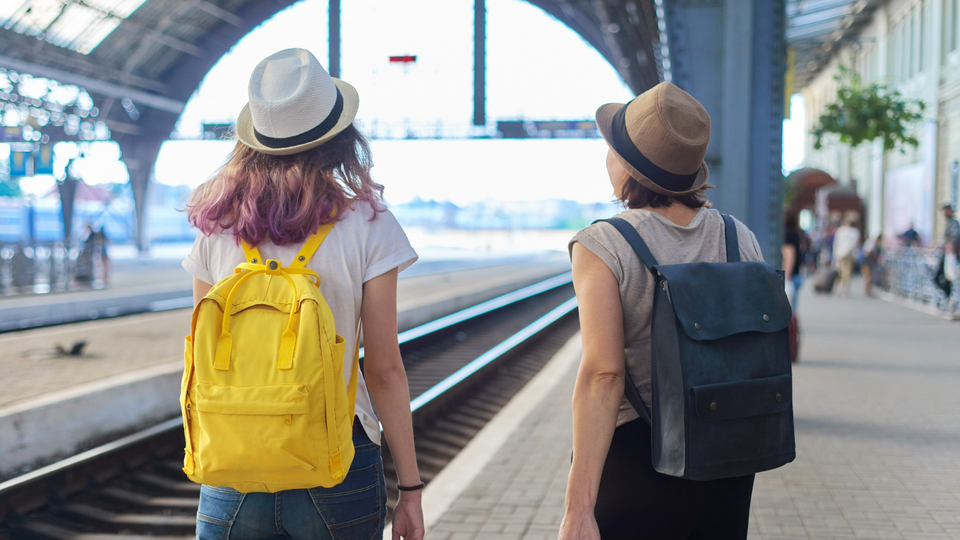 Two young women wearing backpacks at a train station