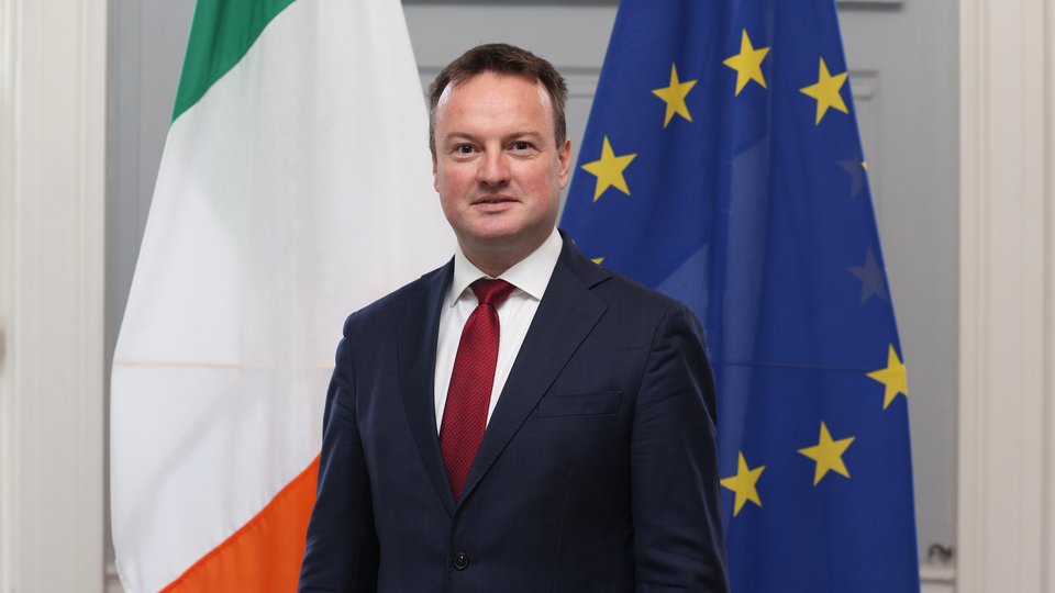 Ein Mann im Anzug vor der irischen und der europäischen Flagge