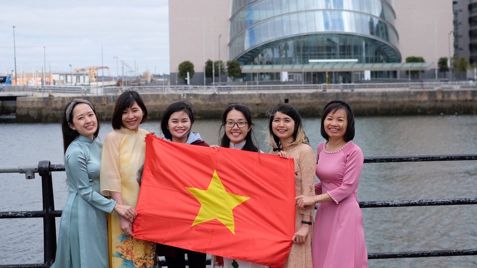 Students posing for a group photo in front of the Convention Centre in Dublin with the Vietnamese flag.