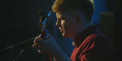 A young man wearing a red shirt playing mandolin in a dark room