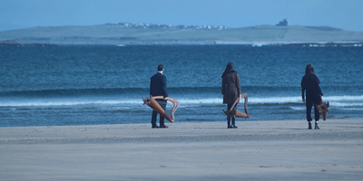 Three people holding harps standing on the beach looking at the sea