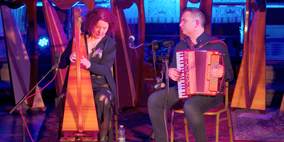 woman playing harp and man playing accordion on stage with pink lighting