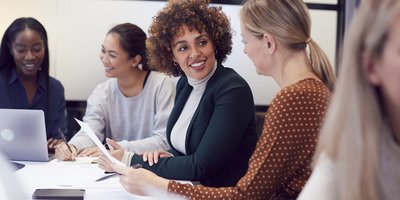 Women sitting at a board table discussing a paper