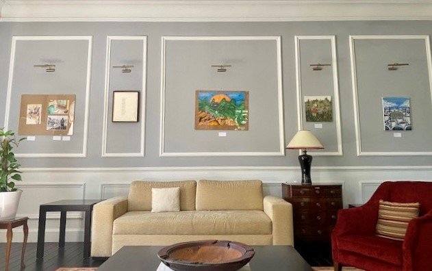 A room with a coffee table and a wooden bowl, an armchair and a sofa, with a number of pictures on the wall.